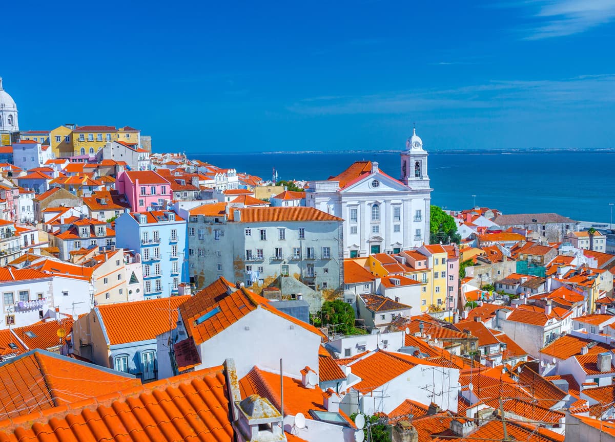 Charming coastal view of Lisbon, Portugal, where colorful historic buildings and iconic red rooftops overlook the Atlantic, all made more efficient with DDD Invoices powering modern digital invoicing solutions.
